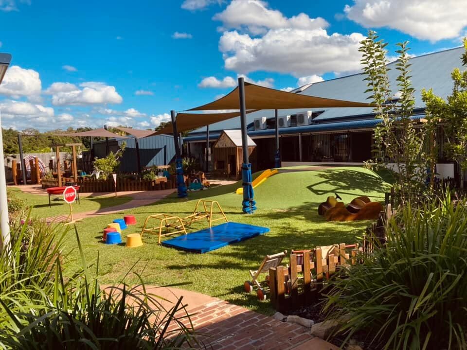 Sun-filled lawn and shade sails in the outdoor play yard at Natural Elements Merrimac