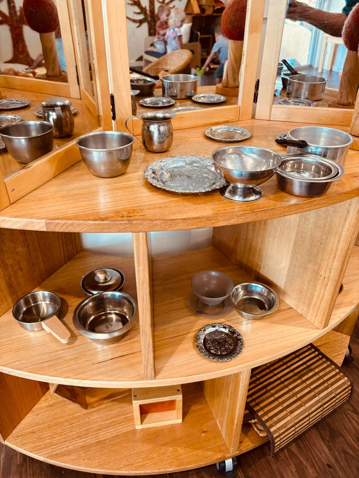 Tiered timber shelves of the mud kitchen with metal bowls and natural loose parts